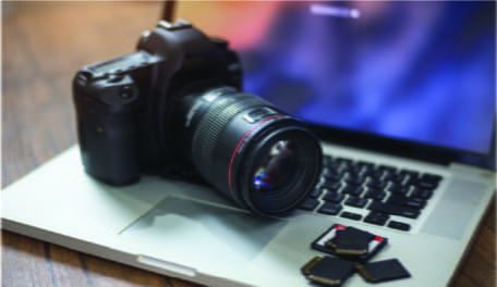 Black DSLR camera sat on silver Macbook laptop with memory cards